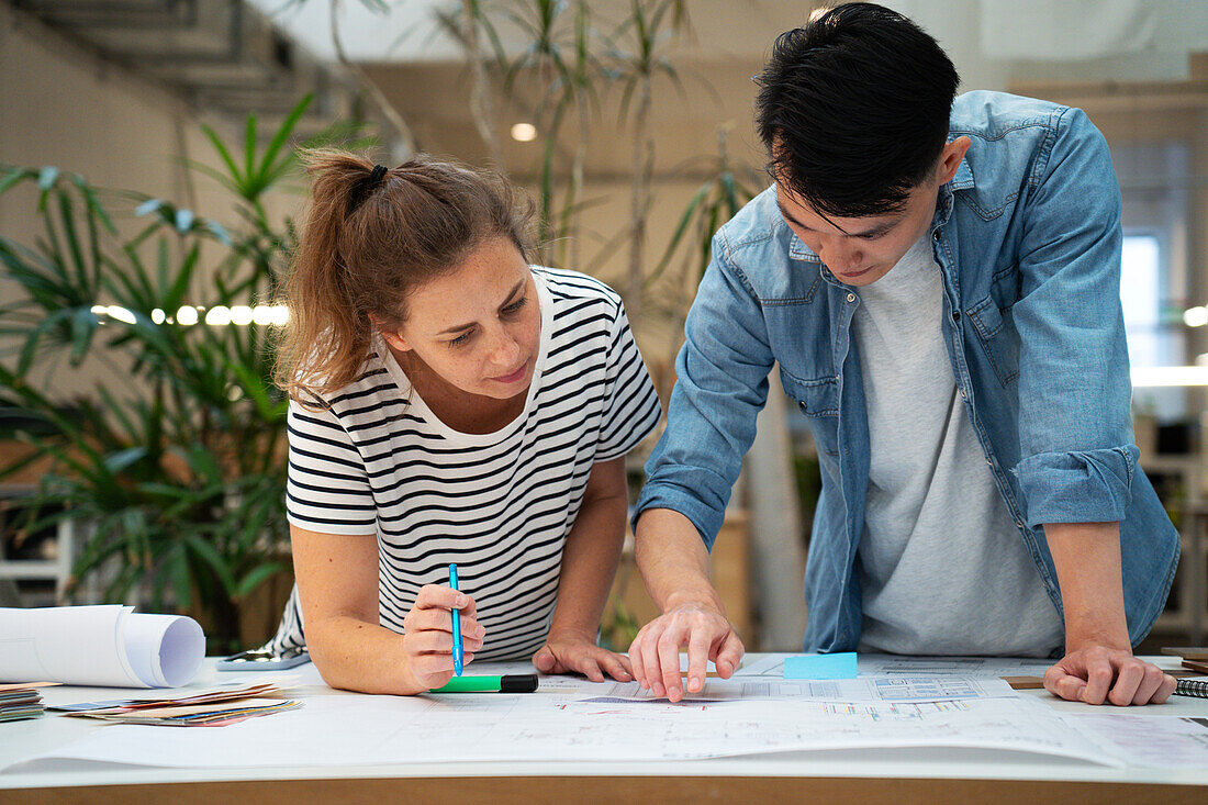 Front view of architects leaning on table while working on blueprints