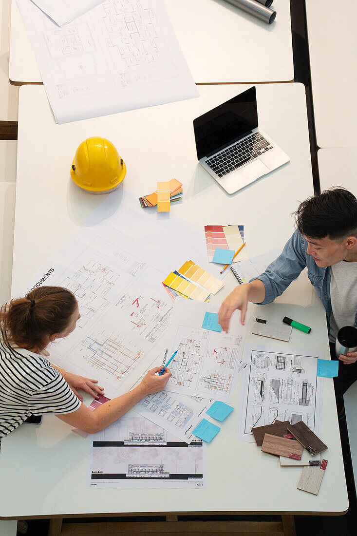 High angle view of civil engineers discussing over blueprints