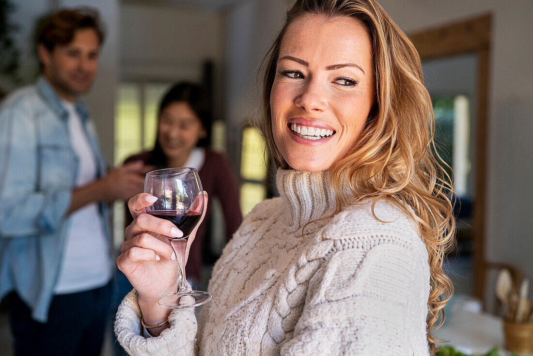 Selbstbewusste Frau hält ein Weinglas in der Hand, während sie mit Freunden auf einer Party sitzt