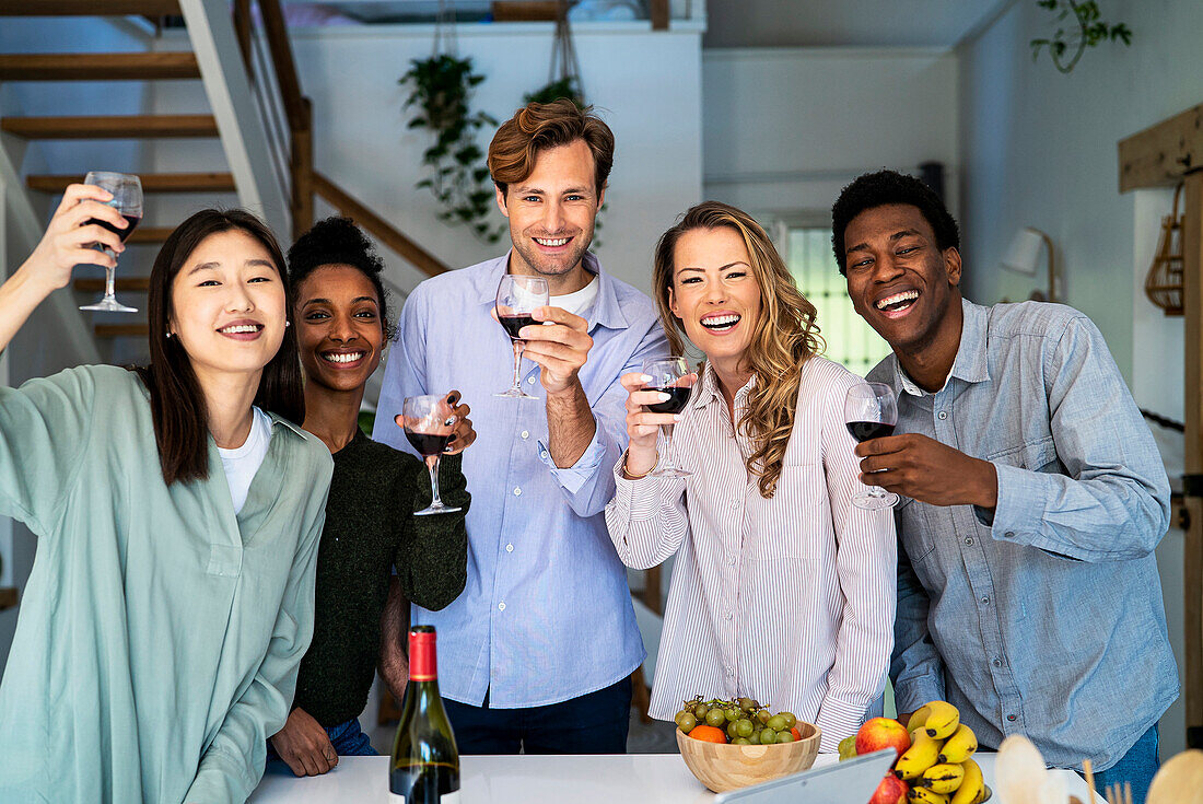 Gruppe von Freunden, die in die Kamera schauen und mit Weingläsern in der Küche anstoßen