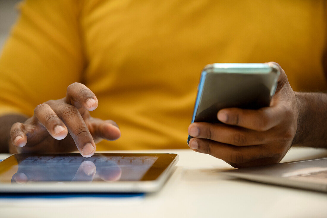 Nahaufnahme eines afroamerikanischen Mannes, der ein digitales Tablet und ein Smartphone in der Hand hält