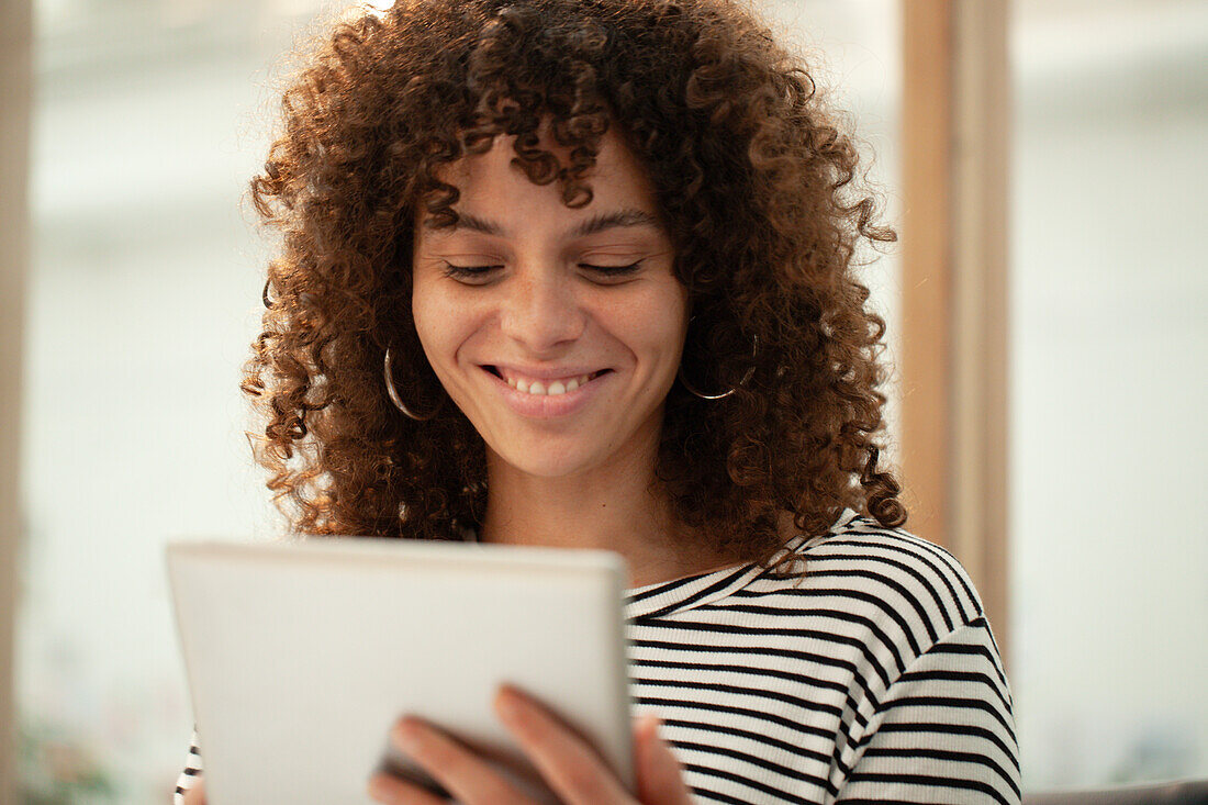 Junge erwachsene Frau lächelt, während sie ein digitales Tablet benutzt