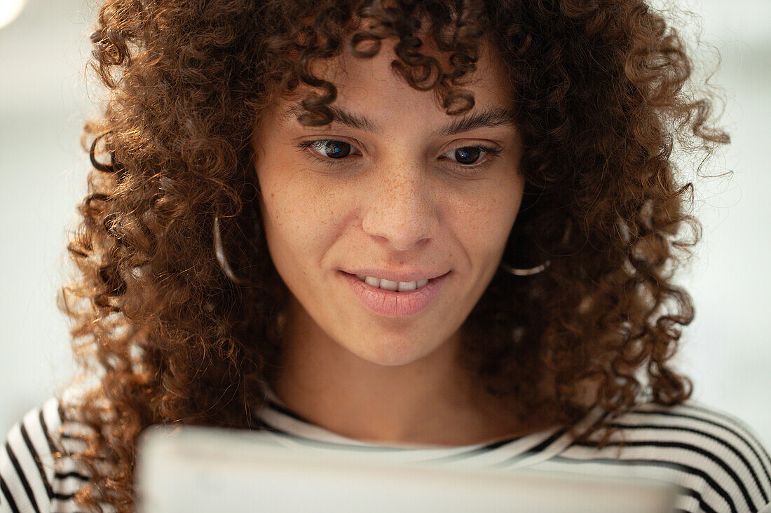 Junge erwachsene Frau lächelt, während sie ein digitales Tablet benutzt