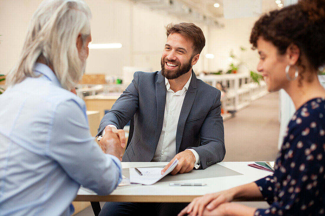 Real estate agent shaking hands with clients after signing contract