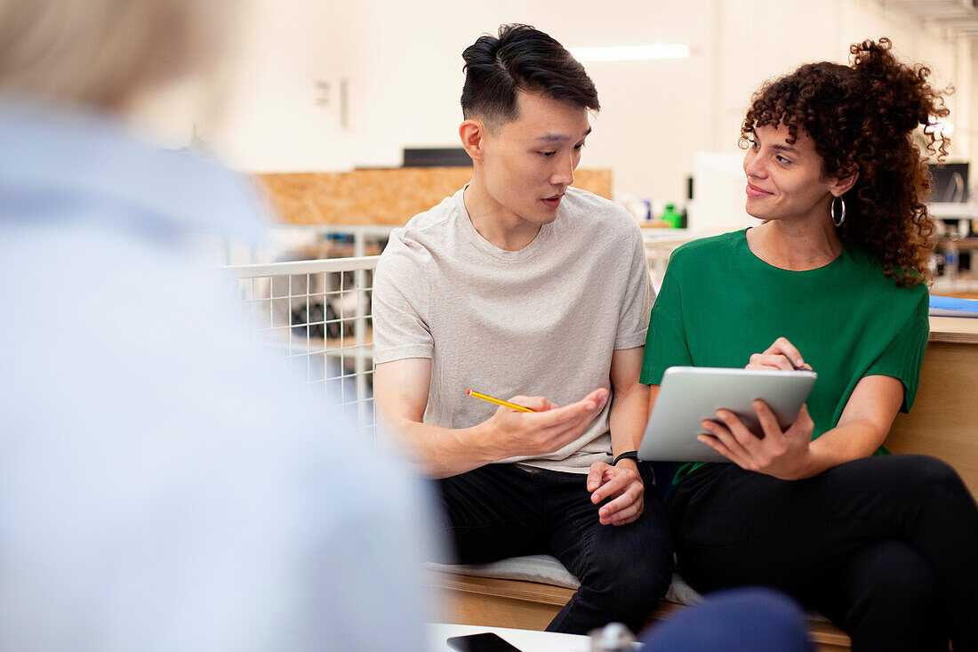 Coworkers discussing over digital tablet while sitting at office