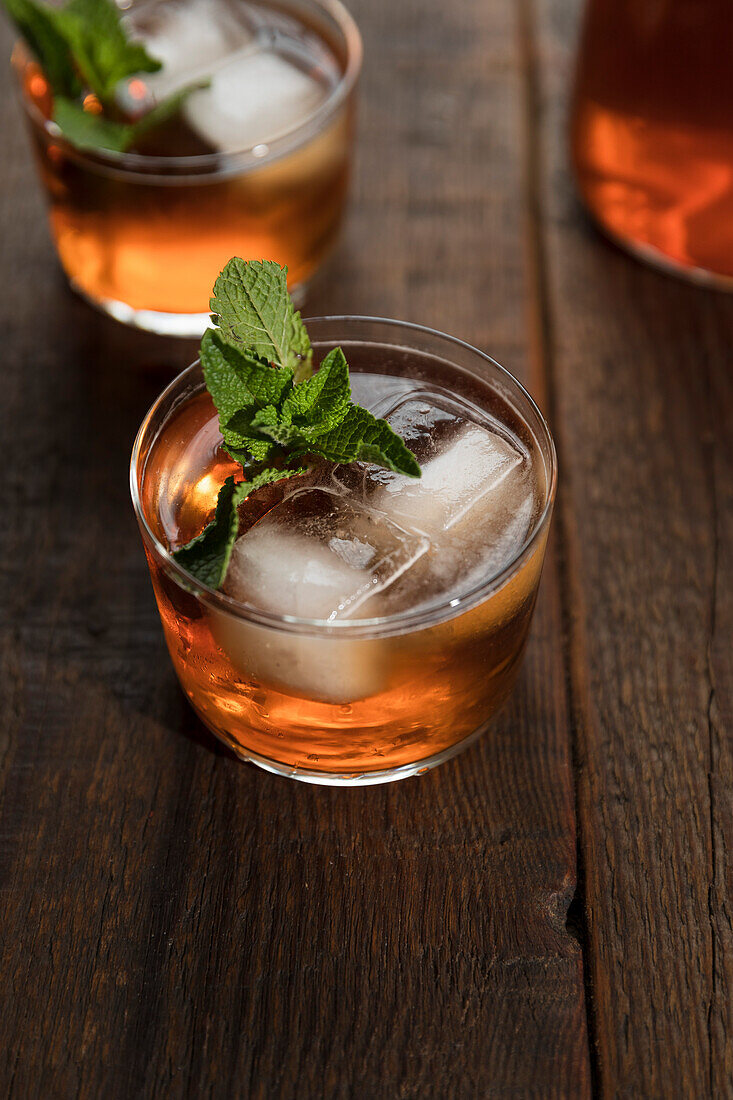 Peach iced tea in a small cup with ice cubes and fresh mint leaves