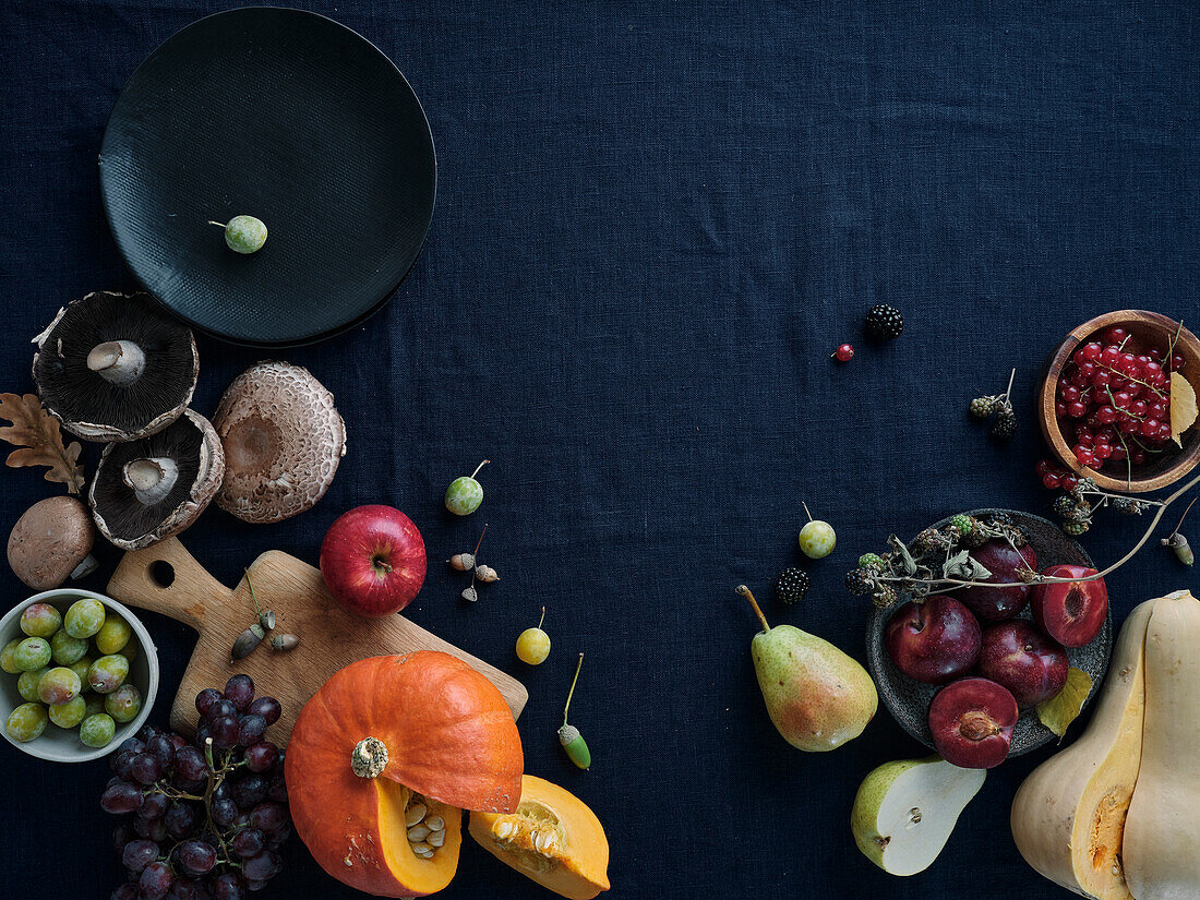 Autumnal food ingredients on dark blue background with copy space. Flat lay of autumn vegetables, berries and mushrooms from local market. Vegan ingredients