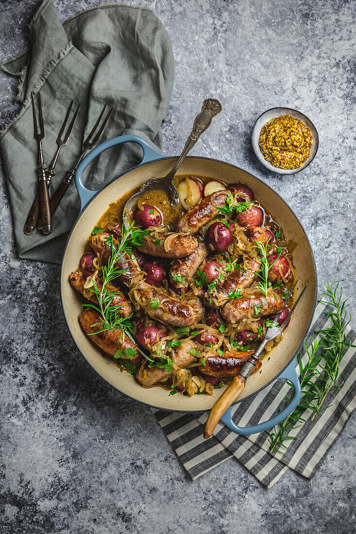 Top view of braised sausage and potatoes in a Dutch oven with mustard in a small bowl