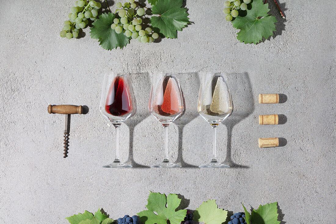 Wine composition with red, rose and white wine in glasses, grape, beautiful sunlight and shadows on grey background. Top view, flat lay. Wine bar, winery, wine degustation concept. Minimalistic trendy photography
