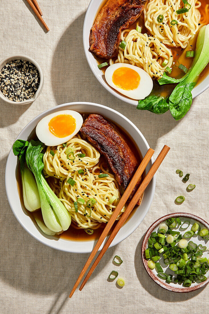 Ramen, pork belly, bok choy and egg against a light-coloured, neutral background