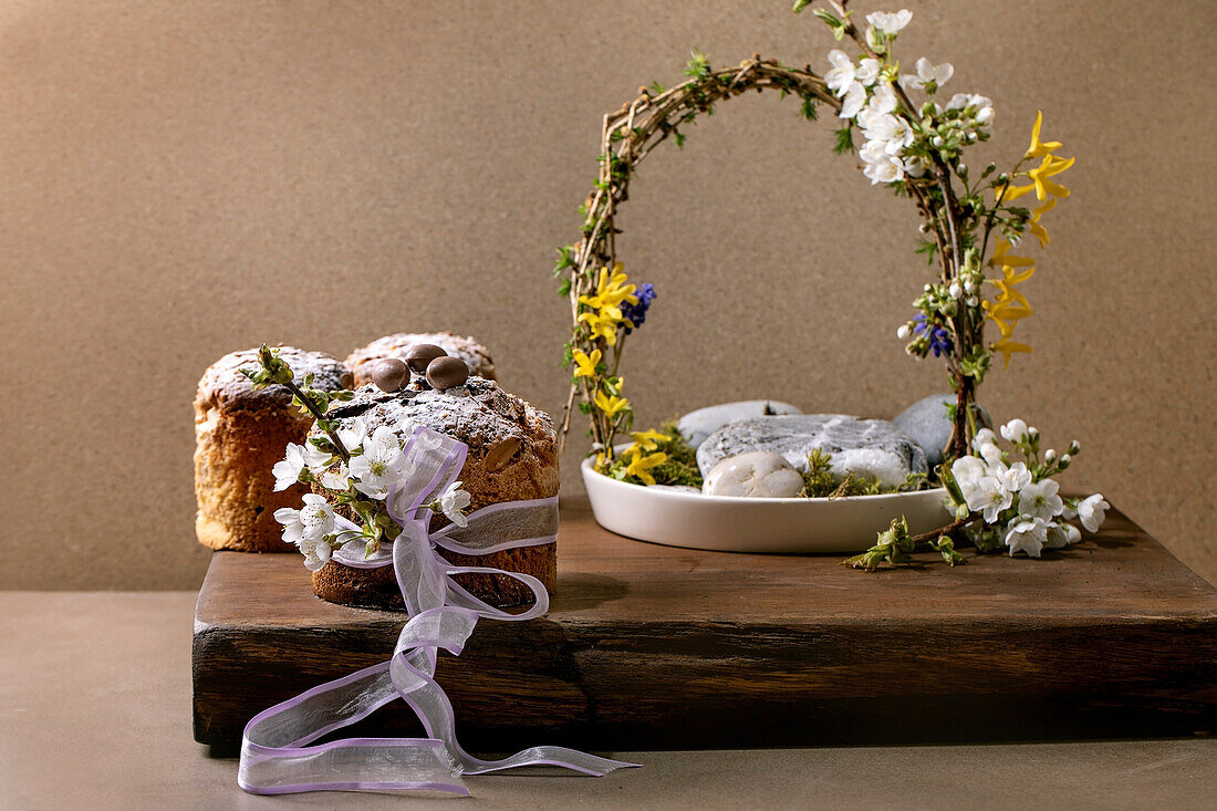 Homemade Italian traditional Easter panettone cakes, decorated by chocolate eggs, pink ribbon and blossoming cherry tree flowers standing on wooden table. Traditional Easter European bake. Copy space