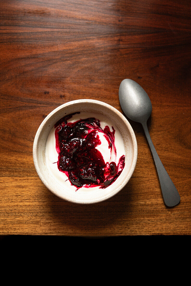 Bowl of yoghurt and blackberry compot on antinque wooden table with silver spoon.