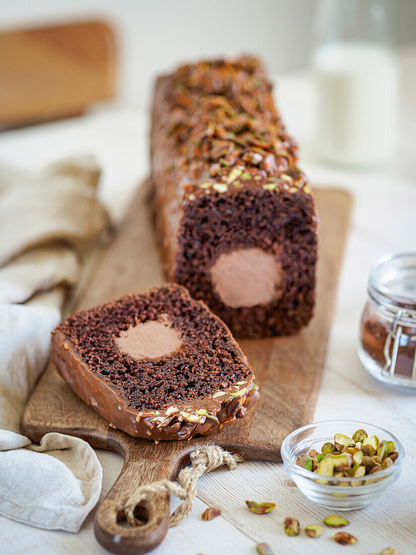 Travel Cake or Tube Cake or Voyage Cake, filled with ganache in the centre and topped with chocolate icing and pistachios (can also be made with peanuts). Chocolate cake with chocolate cream cheese filling in the centre. Idea and recipe for baking with ganache cream centre. Loaf cake on women's hands