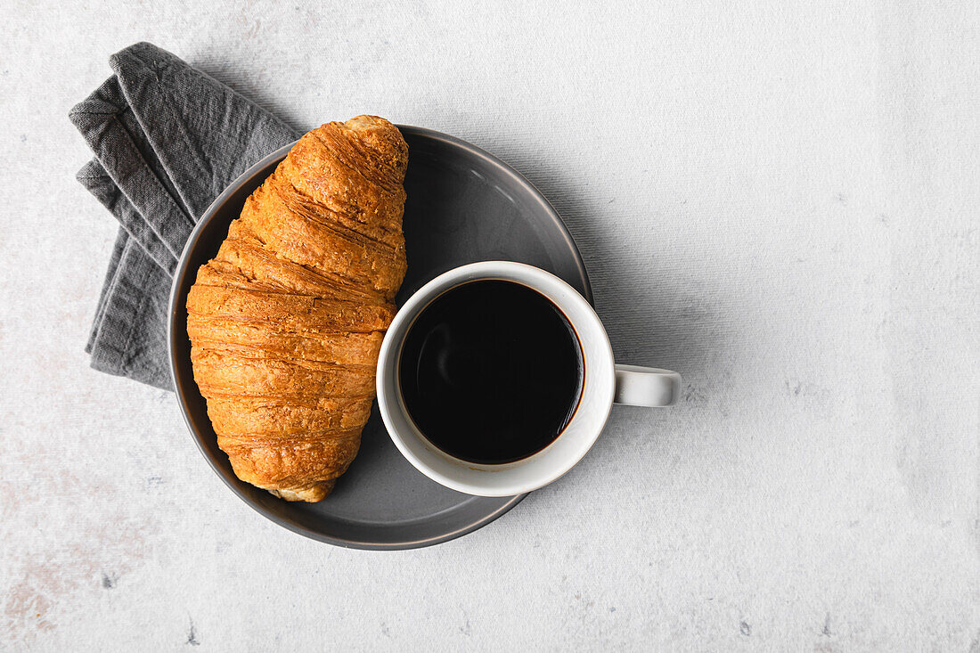 Tasse Kaffee und Croissant über Tisch