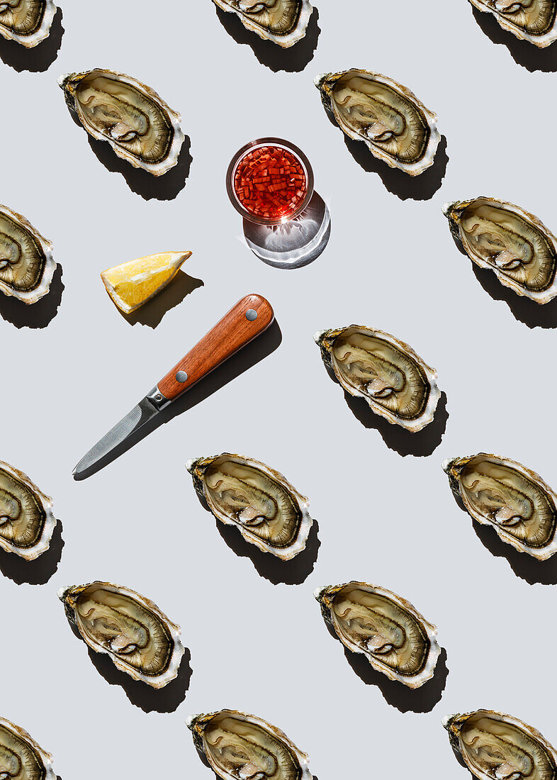 Open Fin de Claire oyster, lemon, sauce and knife on grey background pattern