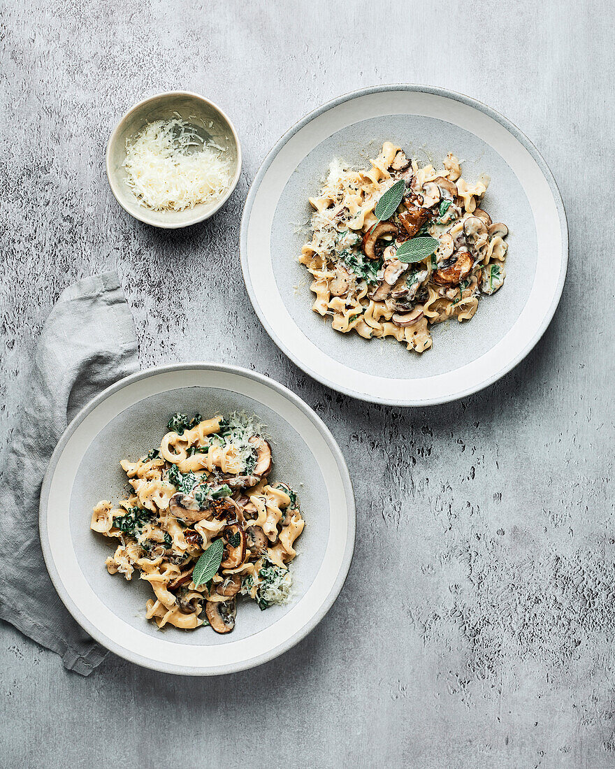 Two bowls of creamy mushroom pasta on a grey background with grey napkin