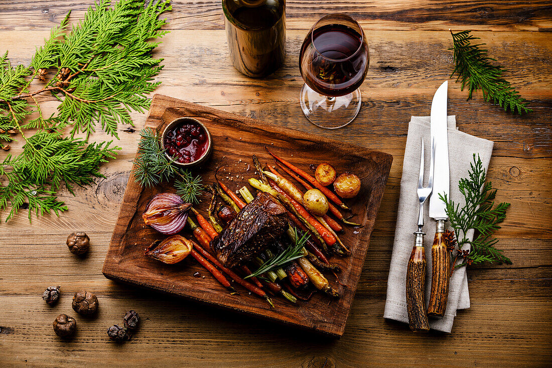 Grilled Venison Steak with baked vegetables and berry sauce and Red wine on wooden background