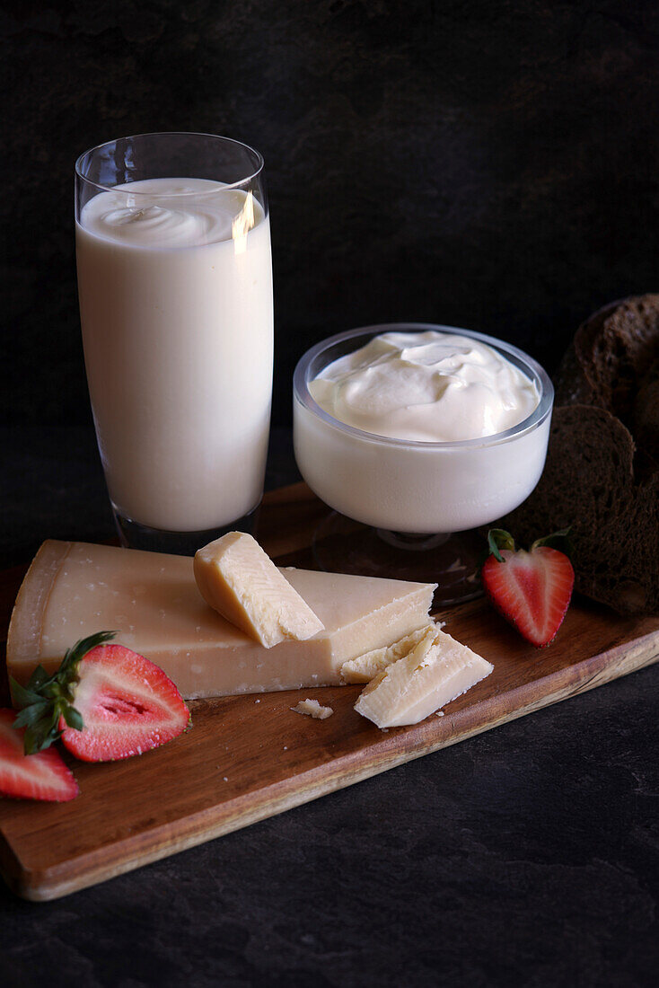Healthy probiotic dairy, including kefir, Greek style yoghurt, and parmgiano reggiano cheese against a dark background.