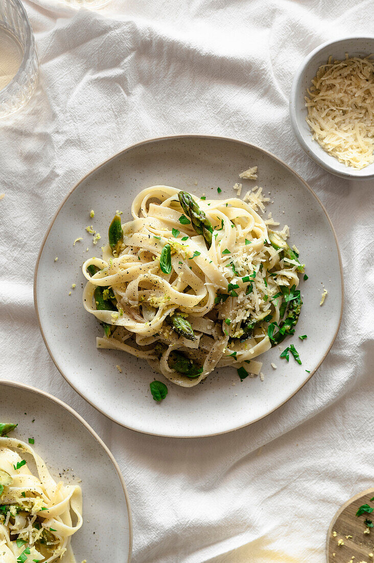 Zitronige Pasta mit Spargel, veganem Käse und frischem Basilikum auf einem frühlingshaften, luftigen Tisch