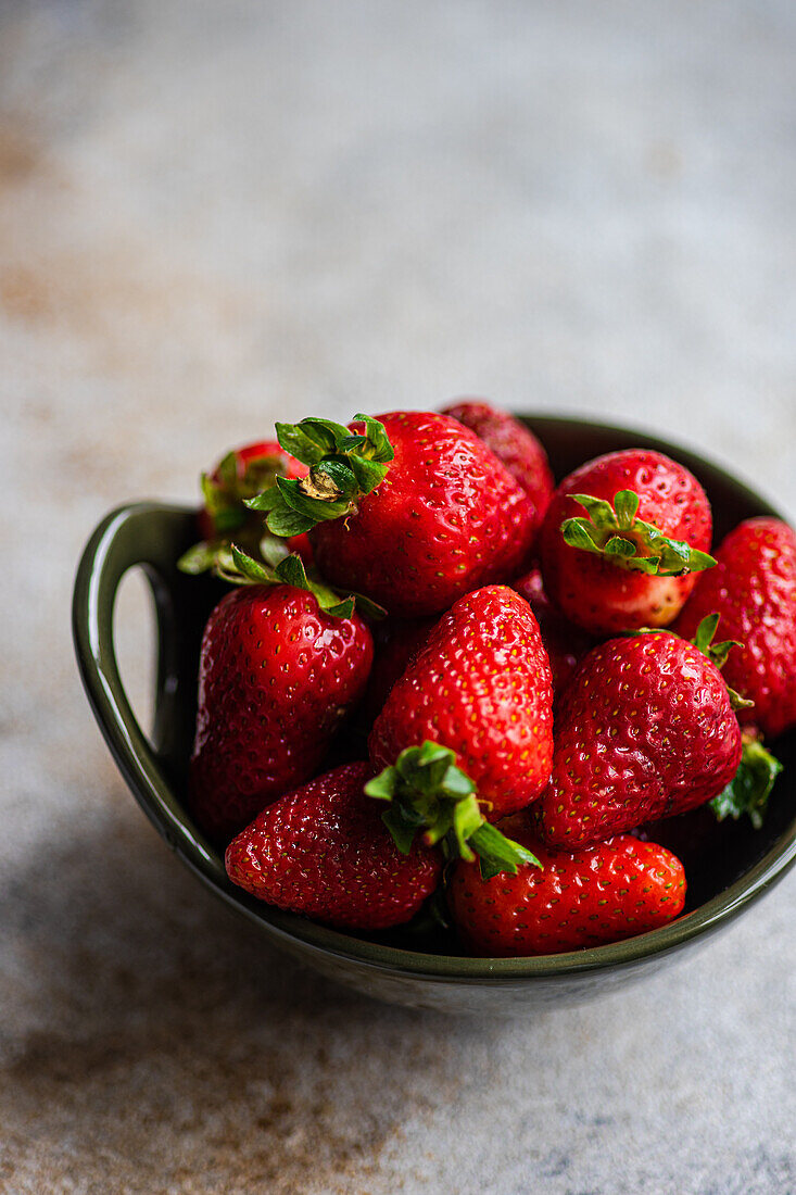 Ripe organic strawberries in ceramic bowl on concrete background