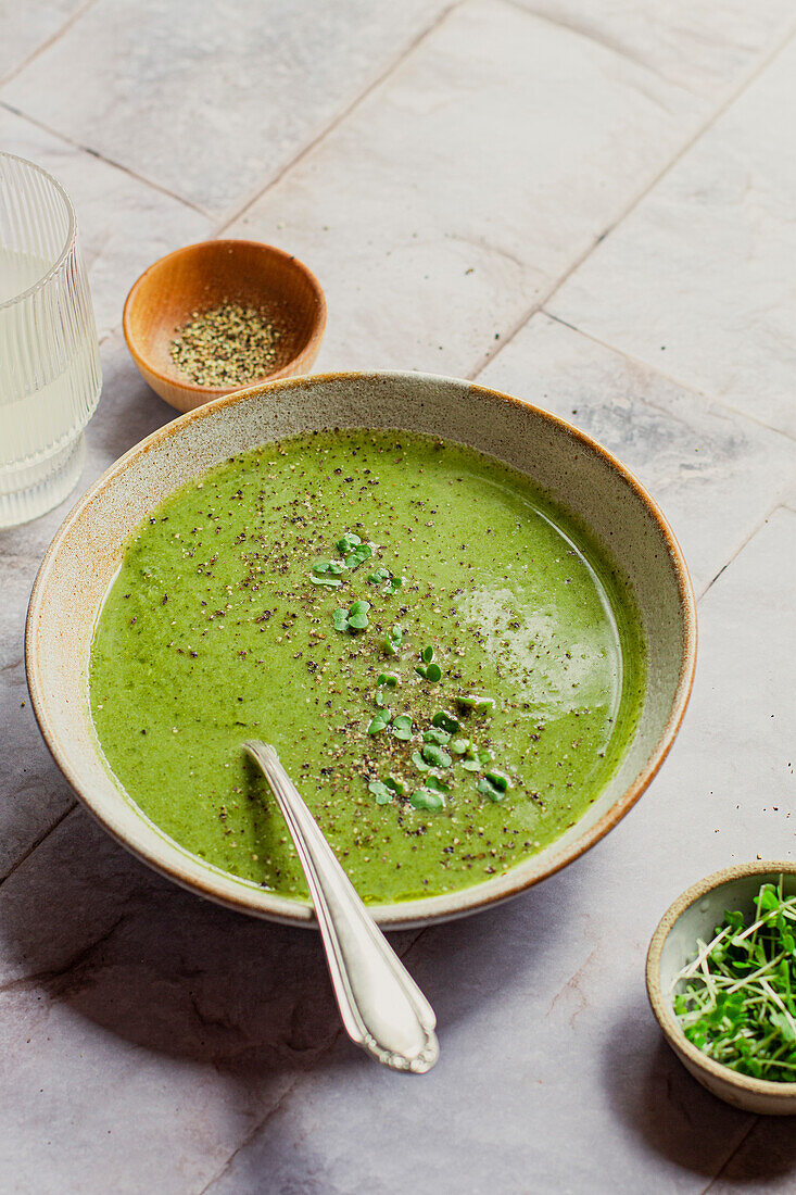 Bowl of green vegetable soup with spoon, garnished with black pepper and watercress