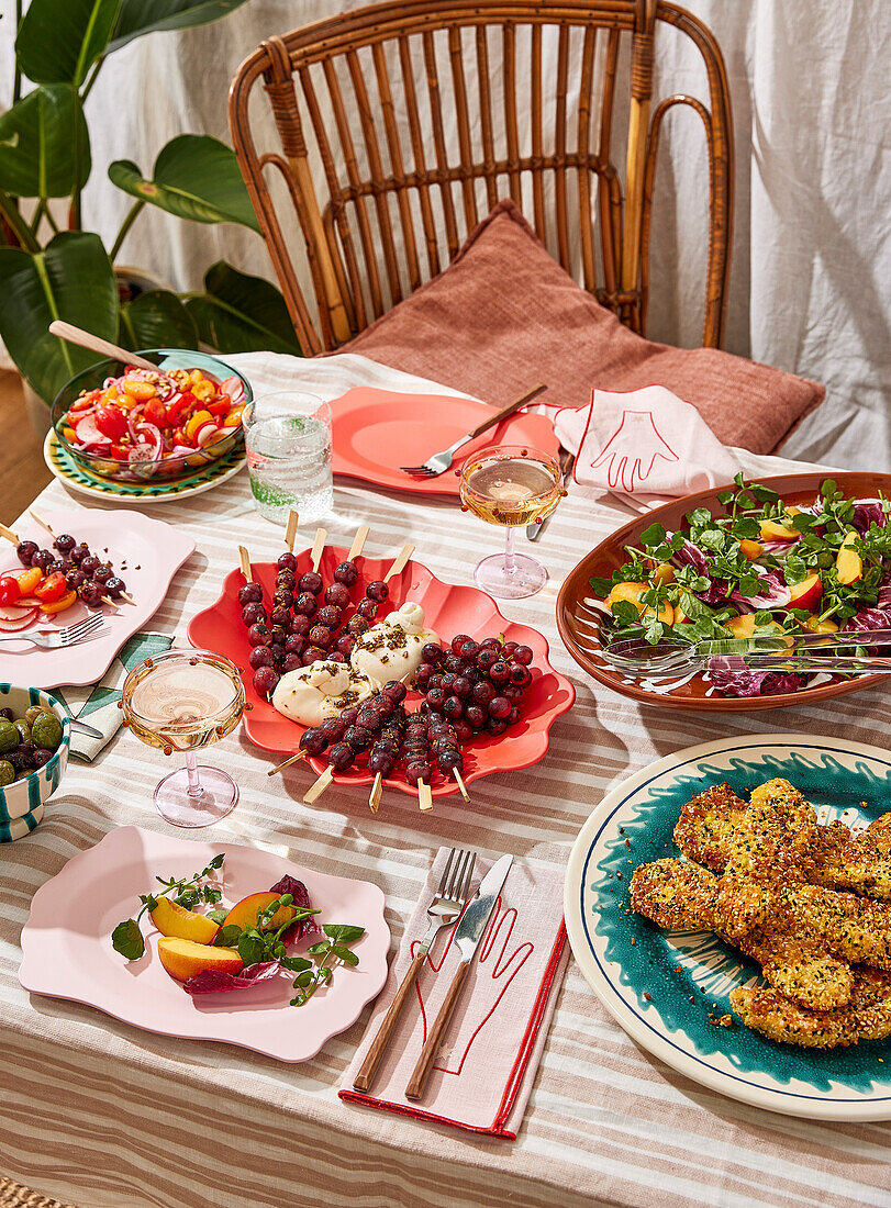 A picnic with salad at an outdoor table, with fresh fruit and fried food, on a striped tablecloth