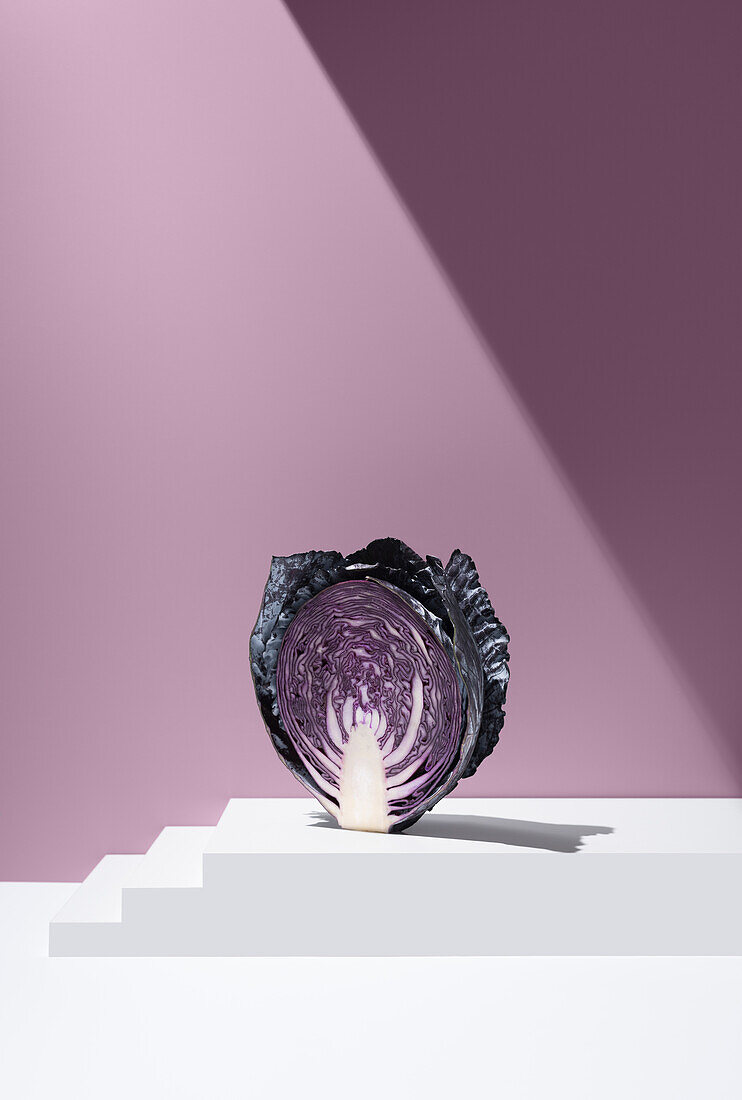 Cross-section of sliced purple cabbage on a white, tiered surface against a purple background in the studio