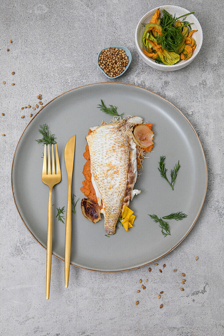 Freshly baked market fish served with fresh vegetables on a grey plate