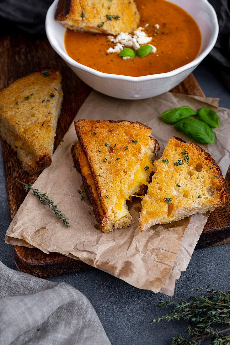 Grilled cheese sandwiches garnished with thyme and a bowl of tomato soup behind them