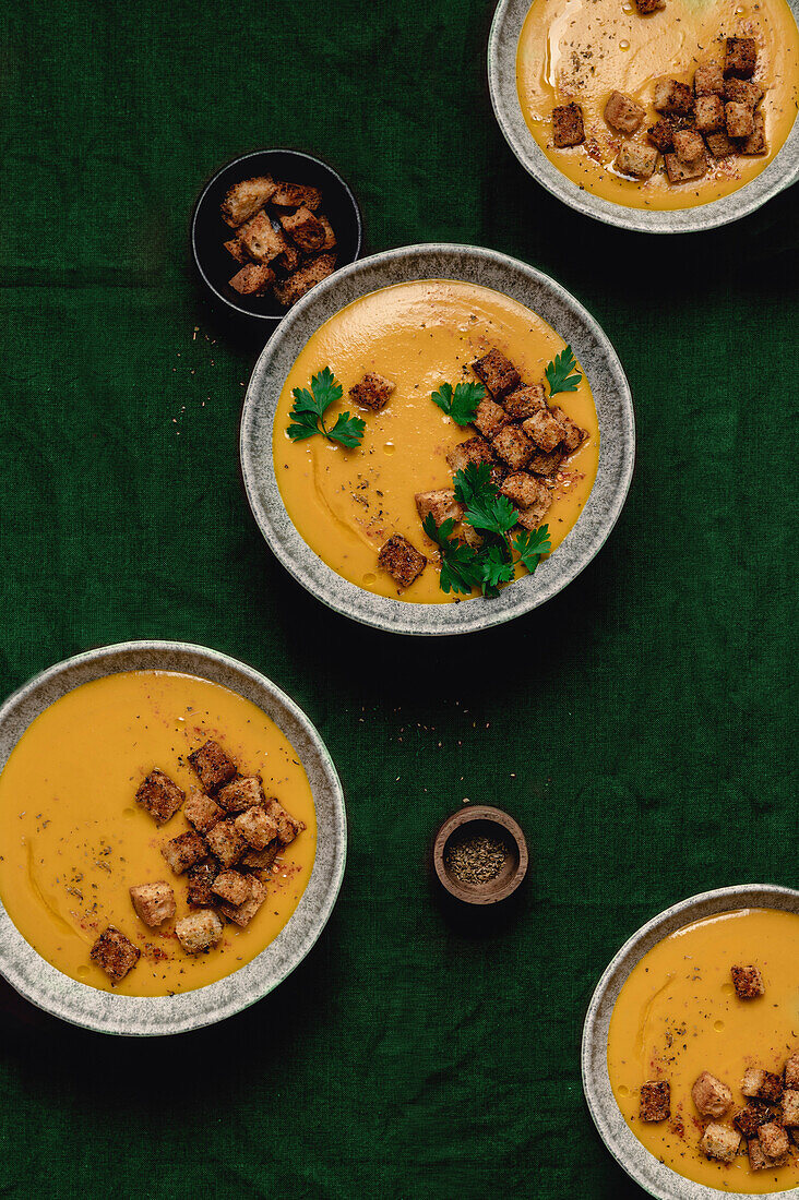 Pumpkin soup plates with bread croutons and fresh parsley in a green table