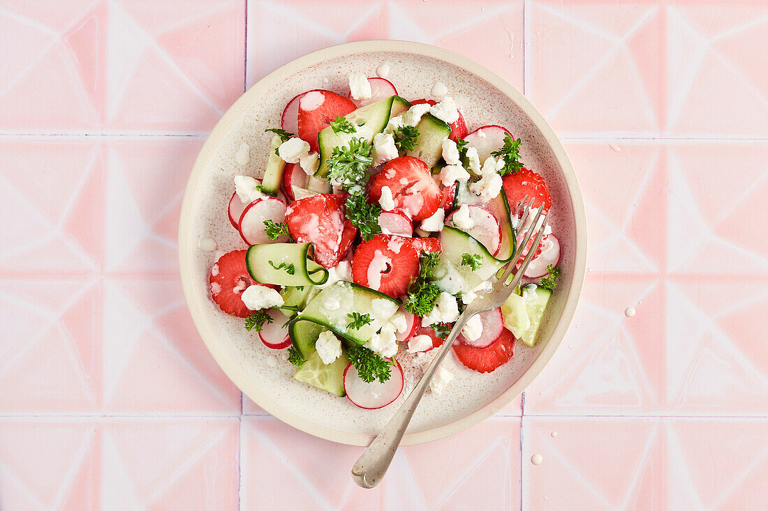 Frühlingssalat mit Erdbeeren, Gurken, Rettich und Petersilie auf rosa Kacheln