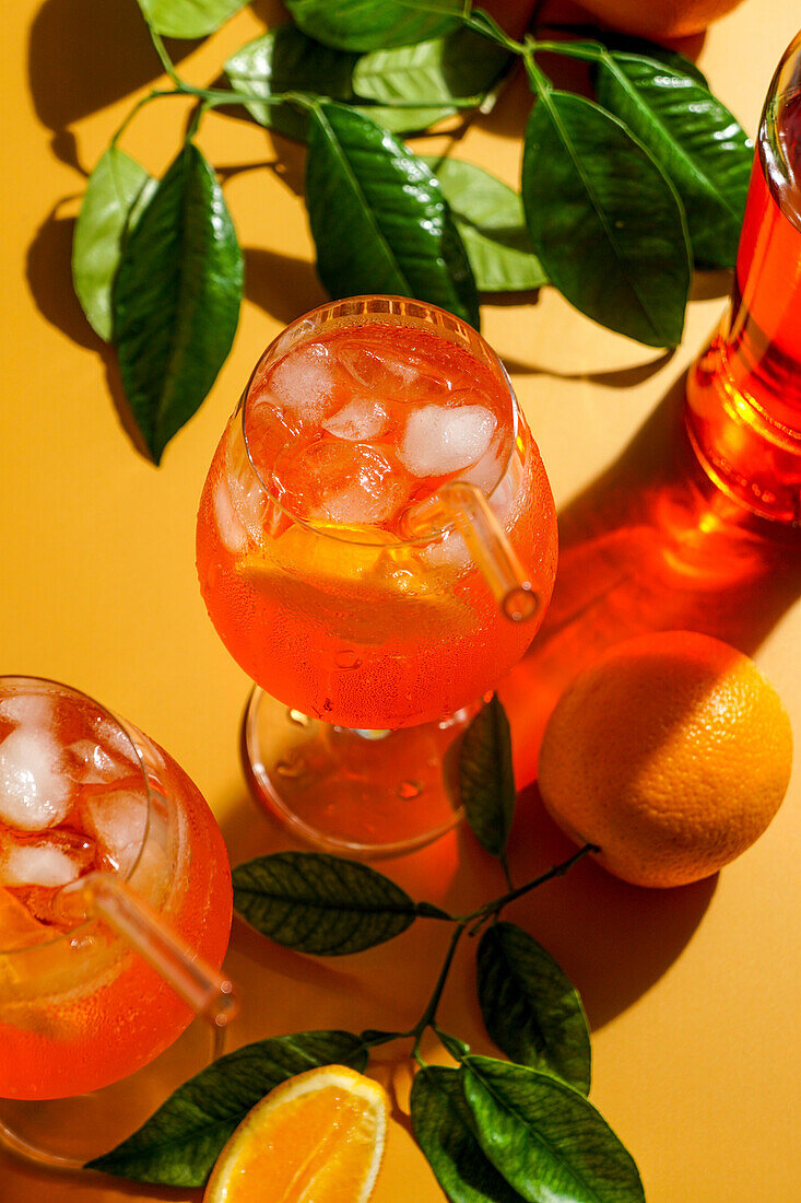 Aperol Spritz Cocktail mit Eis, ein beschlagenes erfrischendes Getränk, auf einem orangefarbenen Hintergrund, Sonnenlicht, Schatten, ein Sommergetränk in einem Weinglas