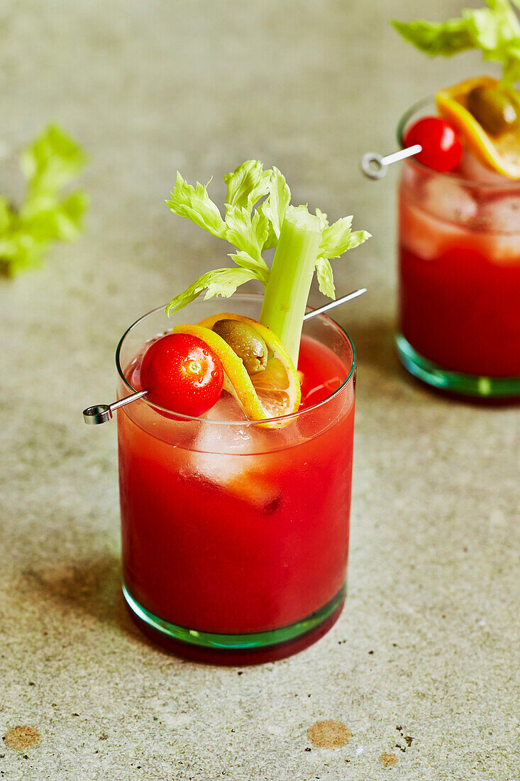 Bloody Mary cocktail with celery, tomato and olive garnish on a sage-green background