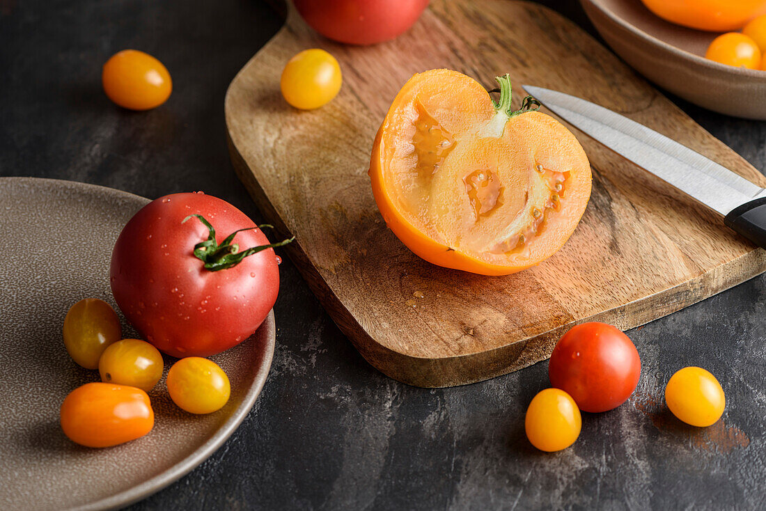 Eine halbe Tomate auf einem Schneidebrett. In der Nähe befinden sich verschiedene gelbe und rote Tomaten