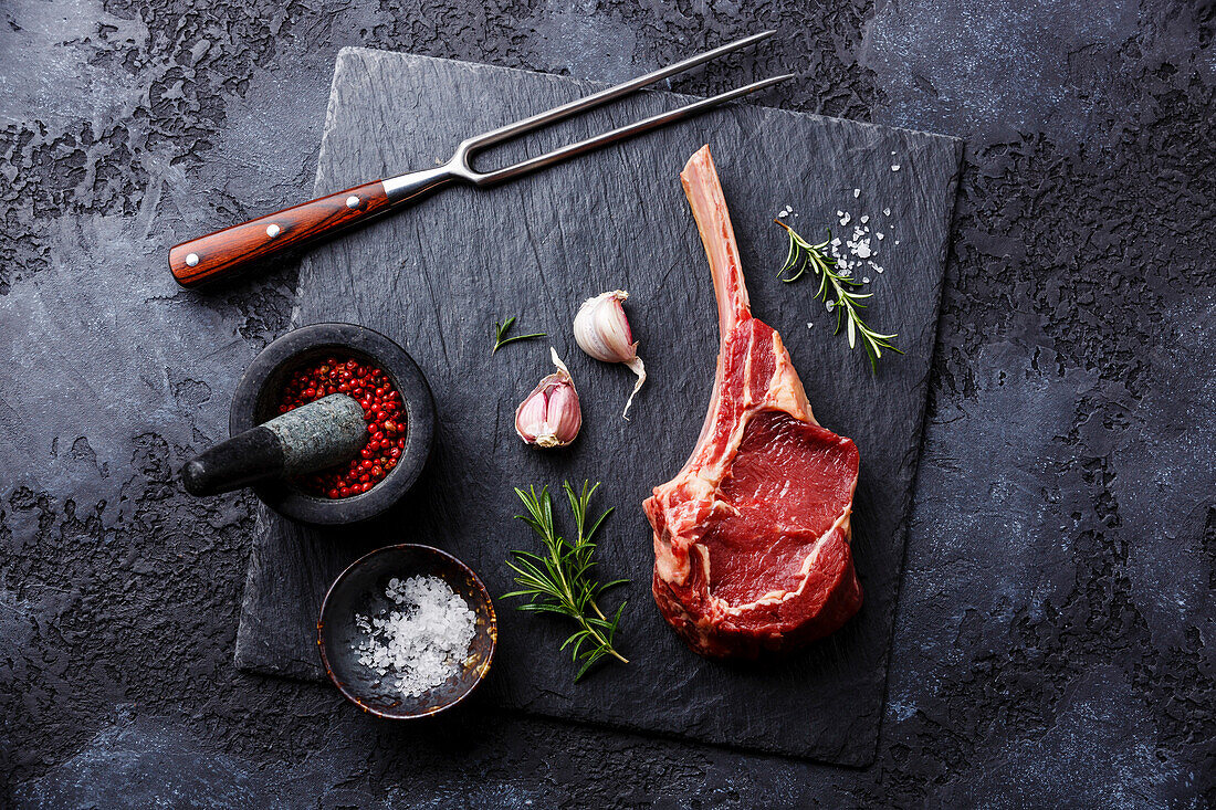 Raw fresh meat veal ribs and spices on a black stone plate on a dark background