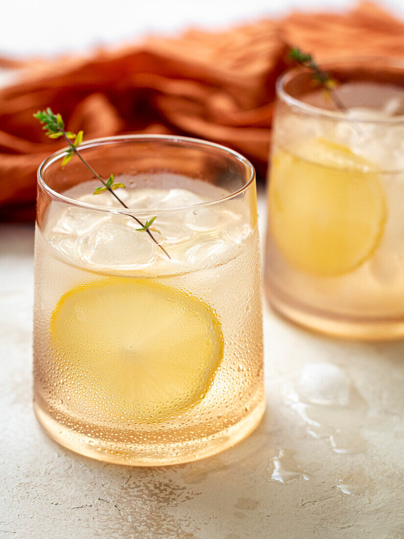 Glas Wasser mit Eiswürfeln, dekoriert mit einer Zitronenscheibe und Thymian