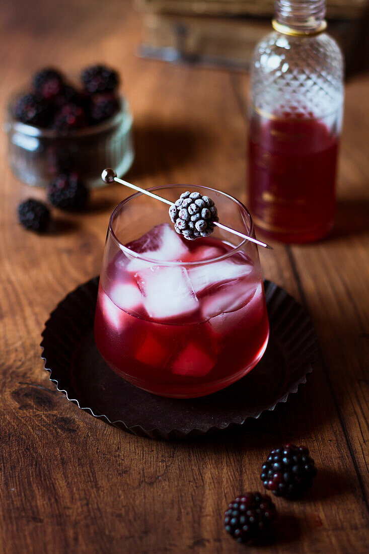 Bramble cocktail with frozen blackberry on a wooden backdrop