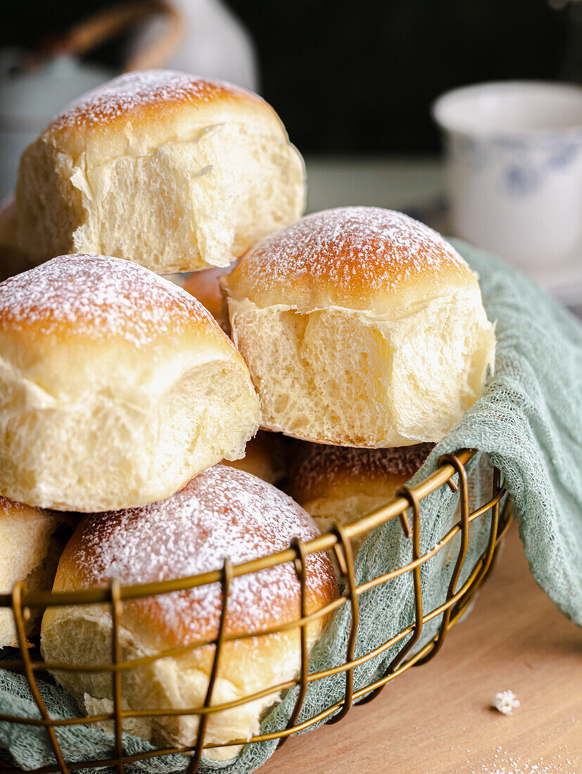 Homemade milk and cream cheese buns in a basket with a cloth next to a window