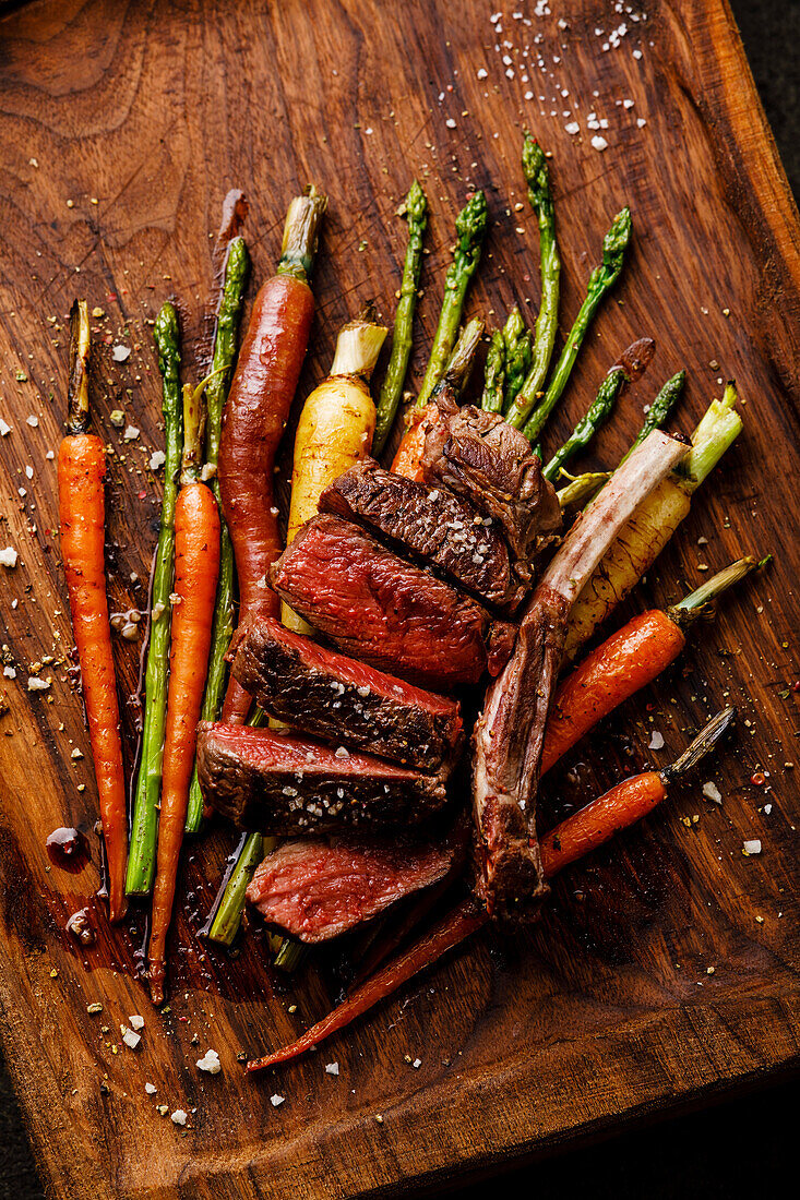 Grilled venison ribs with baked vegetables on a wooden background