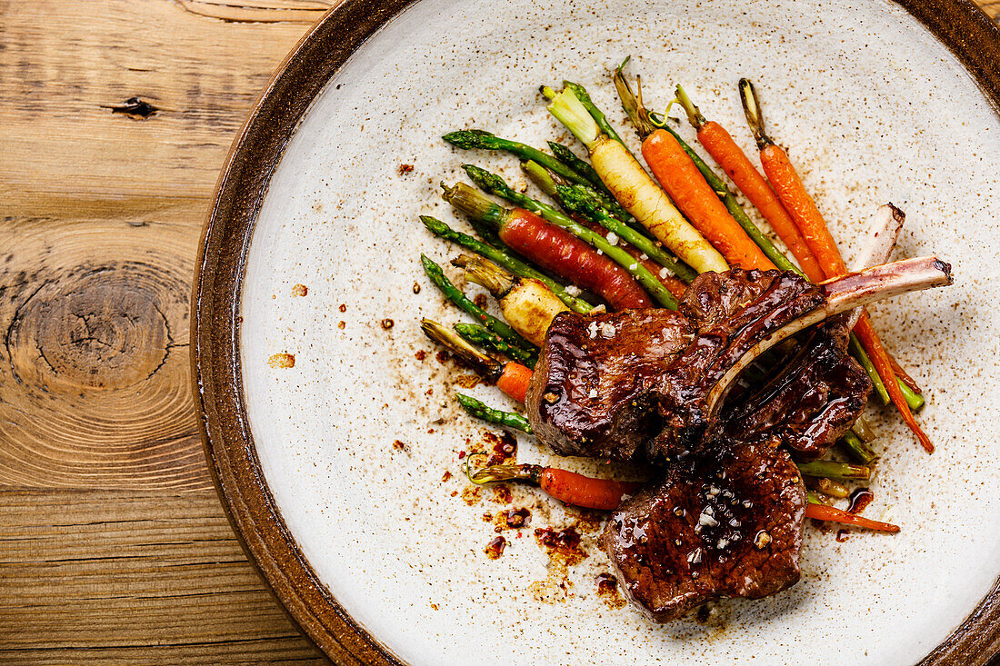 Grilled venison ribs with baked vegetables on a wooden base