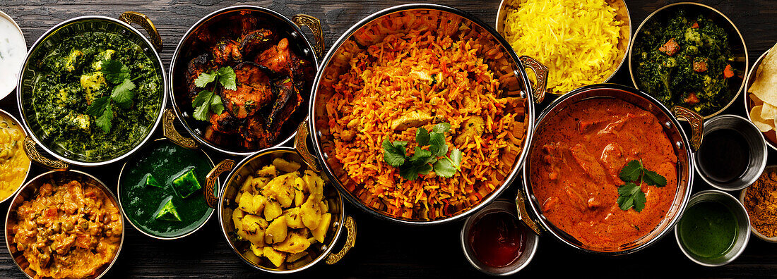 Indian food curry butter chicken, palak paneer, chiken tikka, biryani, vegetable curry, papad, dal, palak sabji, jira alu, rice with saffron on a dark background