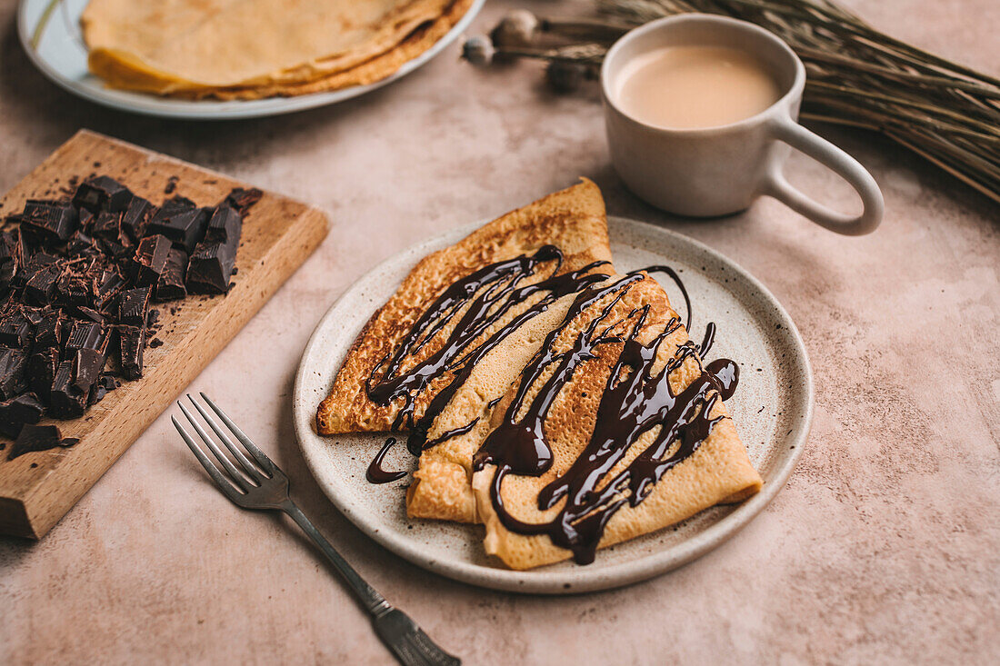 Crêpes drizzled with melted dark chocolate on a ceramic plate