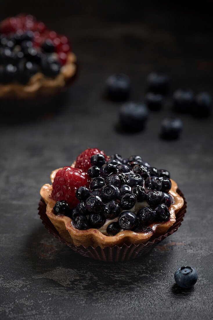 Pastry basket with blueberries and raspberries. Cake on dark background