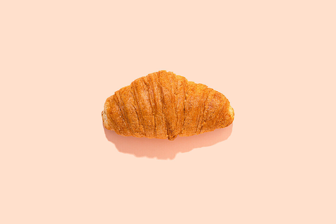 Single croissant in front of pink background