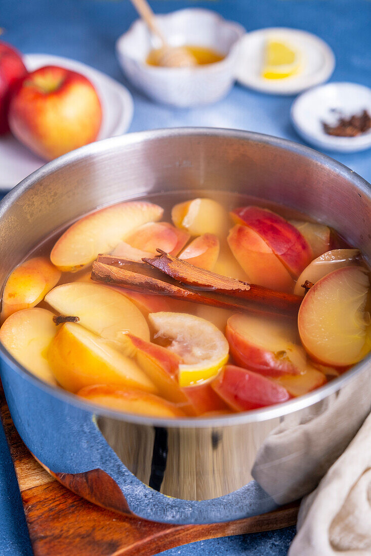 Apple slices cooked in water with a cinnamon stick and cloves in a saucepan.