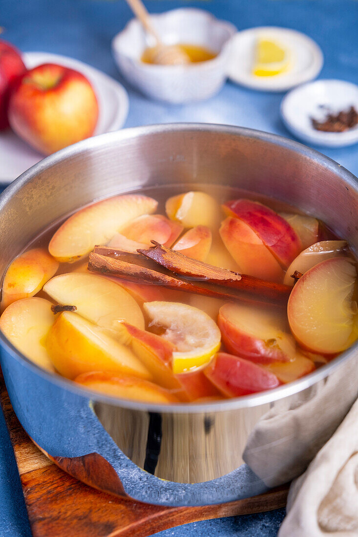 Apple slices cooked in water with cinnamon stick and cloves in a pot