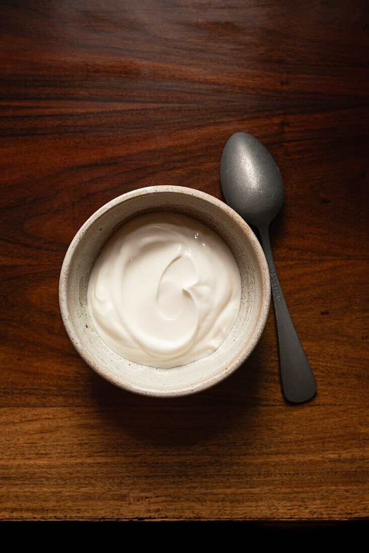 Bowl of yoghurt on antique wooden table with silver spoon