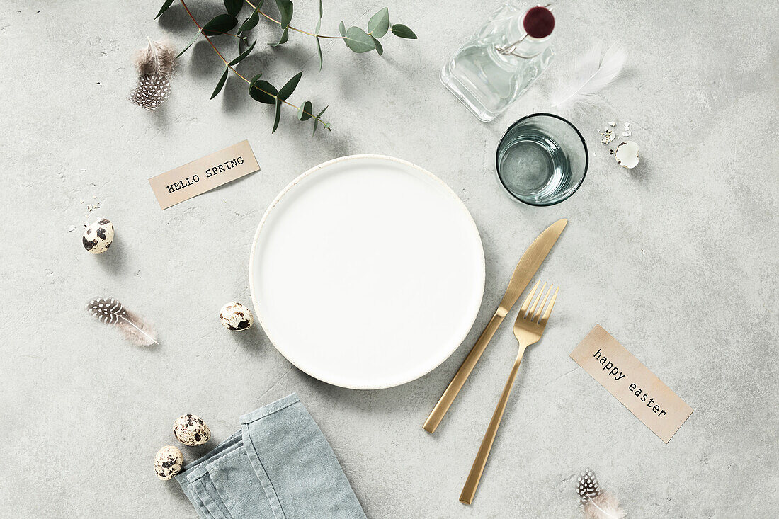 Banner. Table setting. A fashionable minimalistic plate with a linen napkin, Knife and fork, Easter eggs and feathers on a gray background. Top view. Happy Easter holiday concept for cafes and restaurants. Copy space