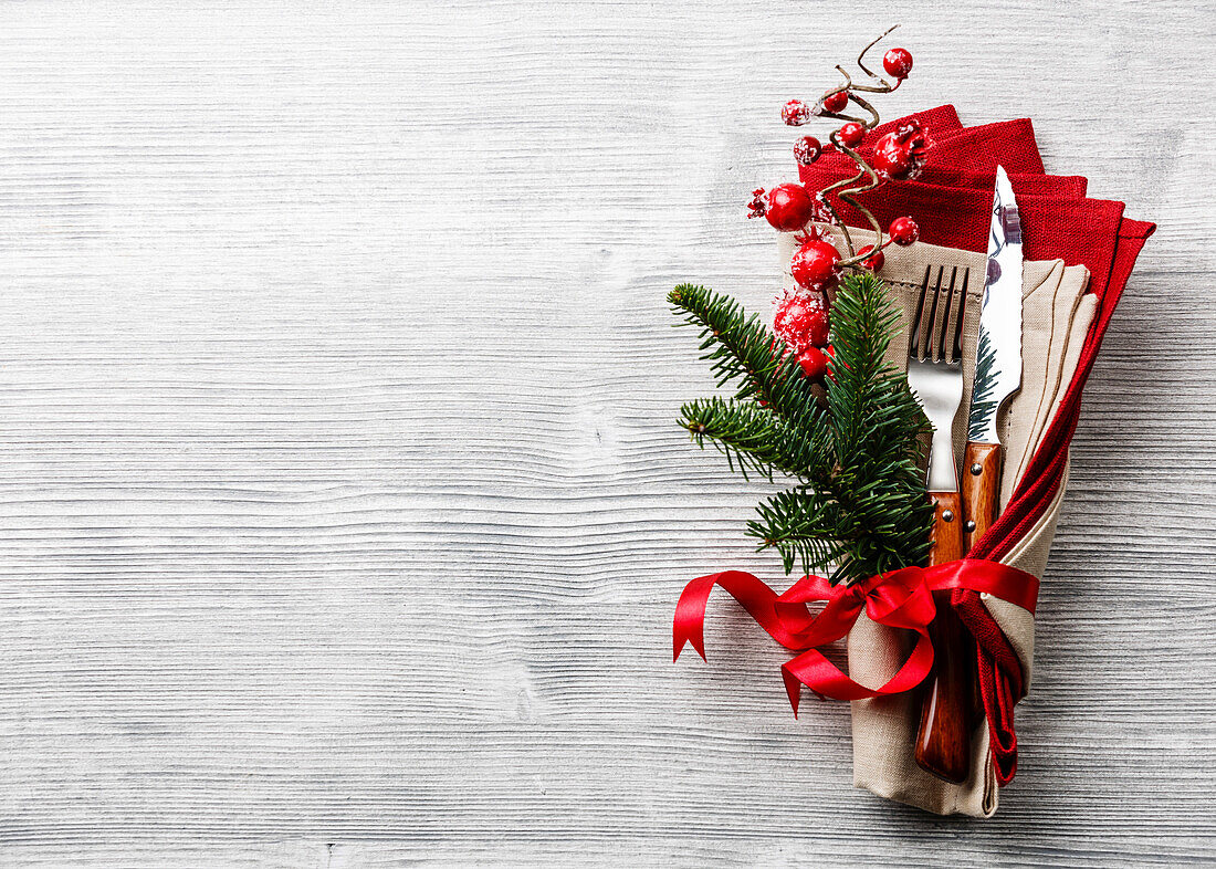 Table fork and knife set with napkin, Christmas fir branch, red berries and ribbon on grey wooden background Copy Space