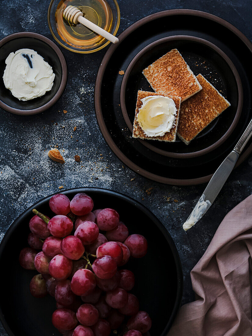 Grapes and cream cheese toasts with honey on black plates